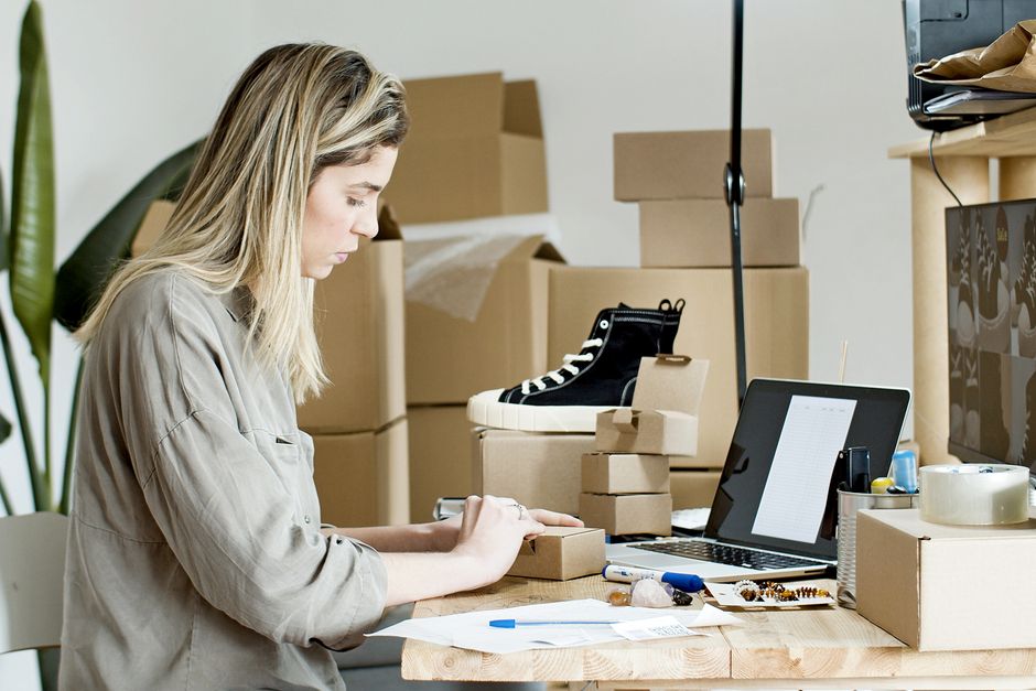 A person packing boxes for an online store, surrounded by packaging materials and a laptop